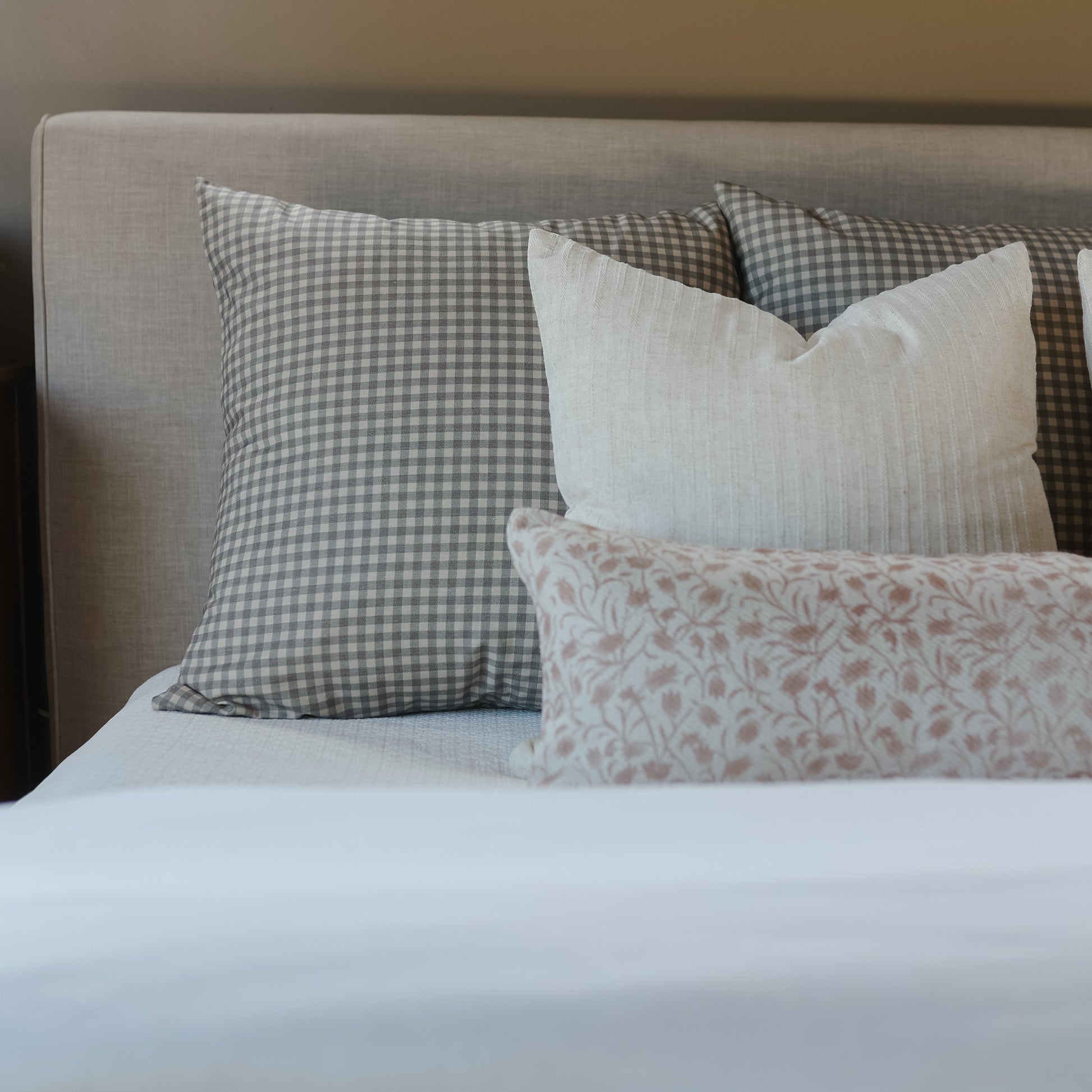 Brown and white gingham check pillow displayed on bed with coordinating pillows and white linens.