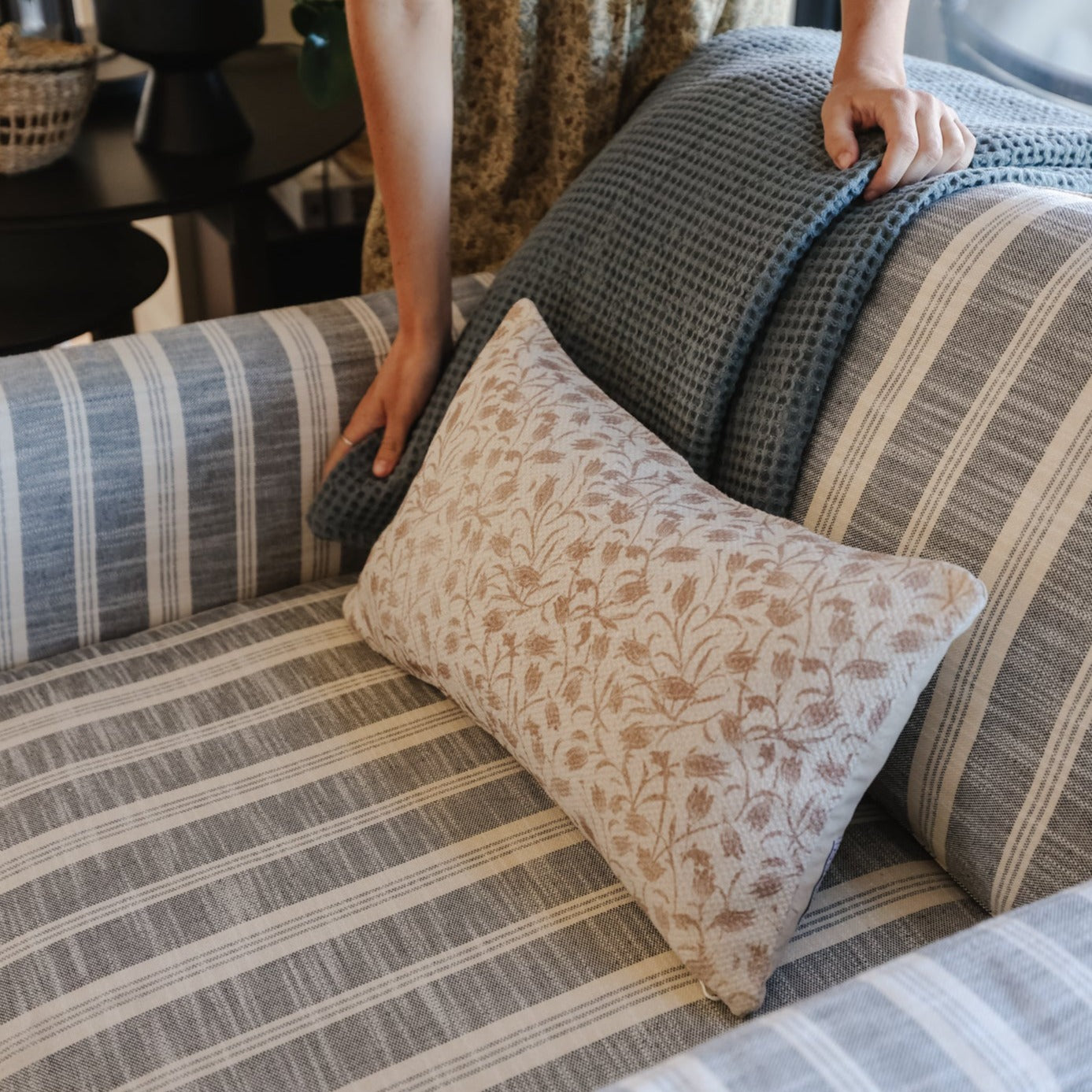 Multiple throw pillows with textured weave fabrics in gray, blue, and tan striped and floral patterns arranged on a couch.