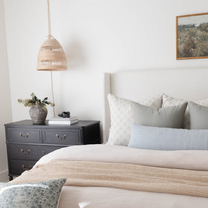Natural woven pendant light with rope suspension hanging above a nightstand in a bedroom setting.