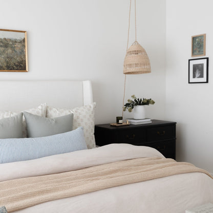 Woven pendant light in natural tan finish hanging above bedroom nightstand.
