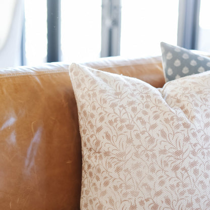 Georgia Thick Weave pillow in cream with leaf pattern displayed on leather chair with blue striped cushions.