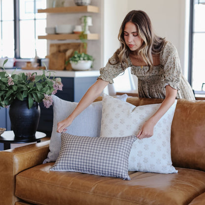 Brown and white gingham check lumbar pillow displayed on a tan leather sofa in a living room setting.