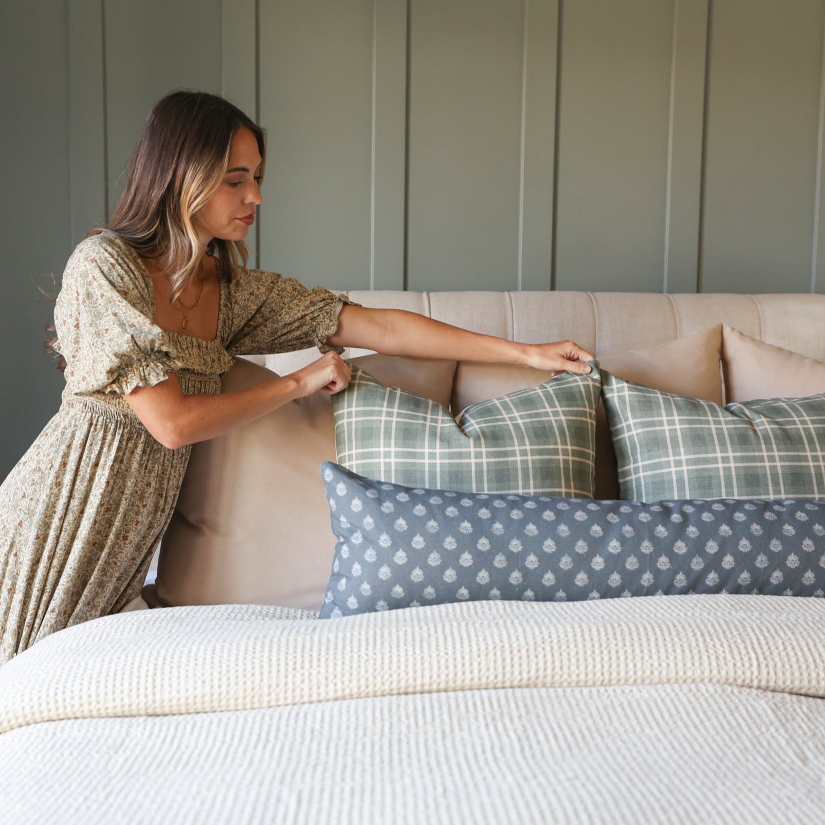 Woman arranging multiple decorative pillows in various patterns and colors on a cream-colored sofa.