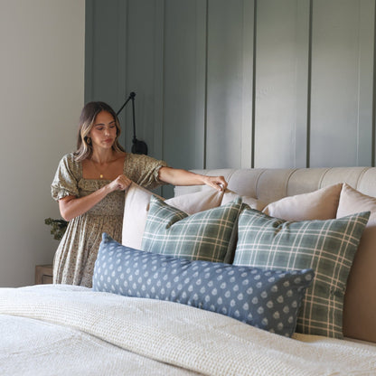 Upholstered bed headboard with vertical channel quilting in sage green, styled with patterned pillows and neutral bedding.