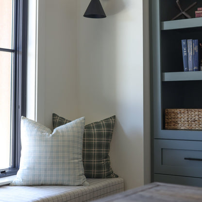 Two plaid throw pillows in blue and olive tones on a light cushioned window seat.