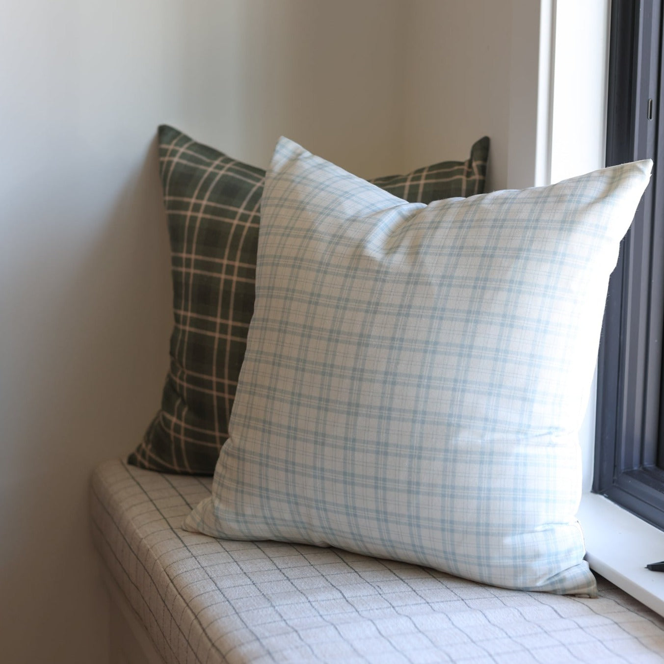 Light blue plaid pillow with dark green tartan pillow stacked on window seat.