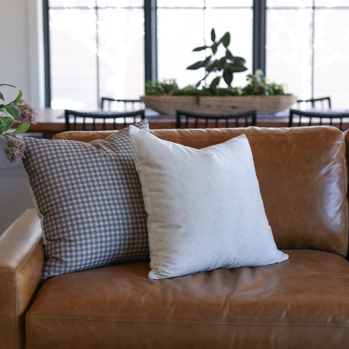 Brown and gray gingham check pillow on tan leather sofa with white pillow.