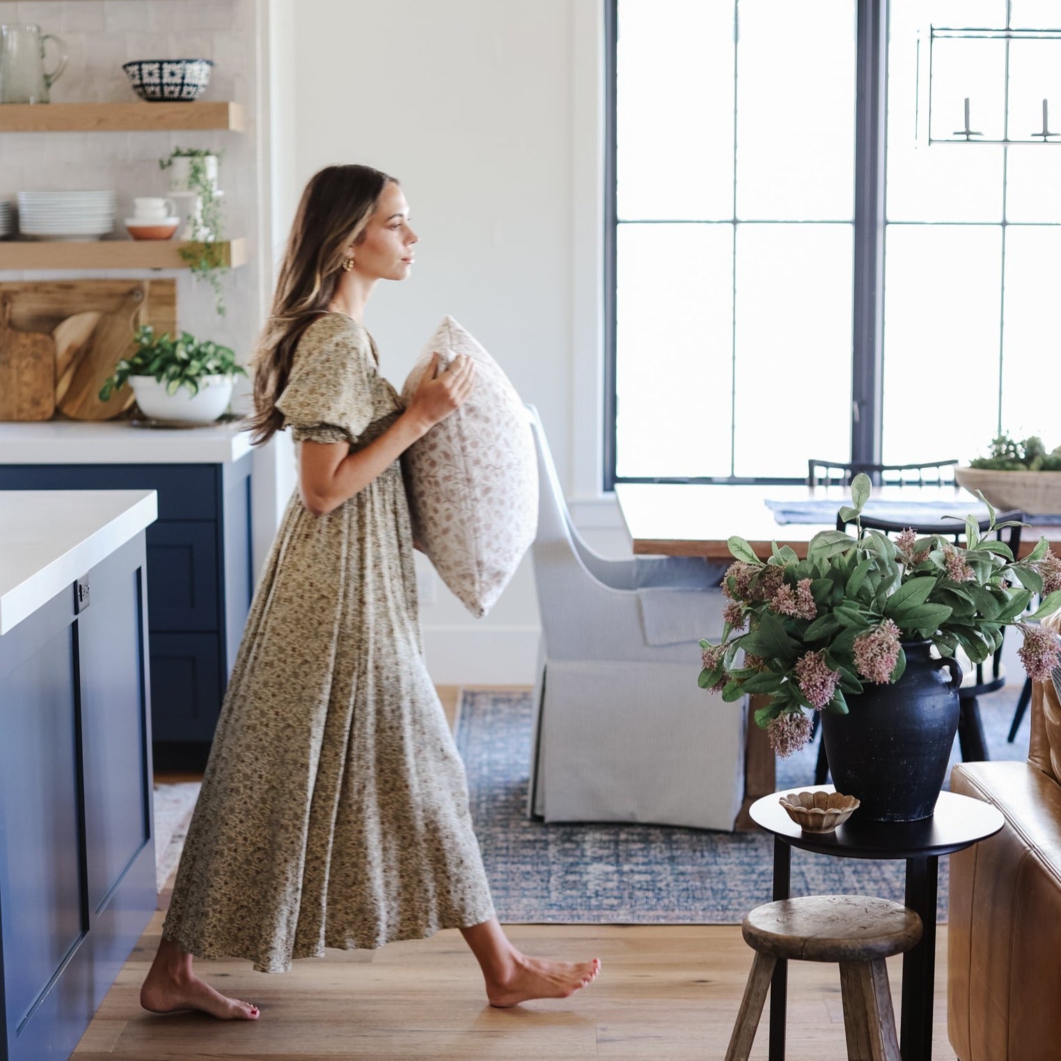Woman holding a cream and gray patterned throw pillow in a modern kitchen and living room setting.