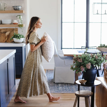 Woman holding a cream and gray patterned throw pillow in a modern kitchen and living room setting.