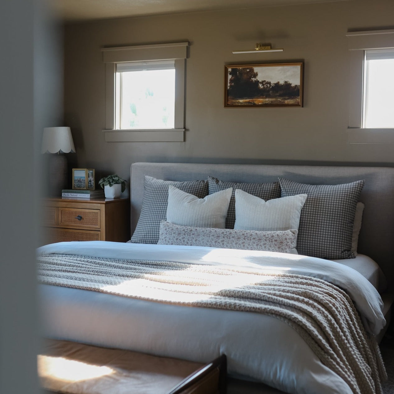 Brown and white gingham patterned pillows and throw blanket arranged on a bed with white and gray bedding.