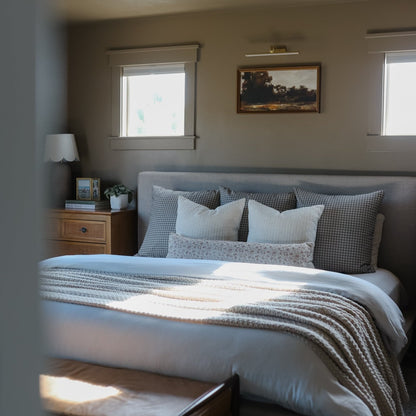 Brown and white gingham patterned pillows and throw blanket arranged on a bed with white and gray bedding.