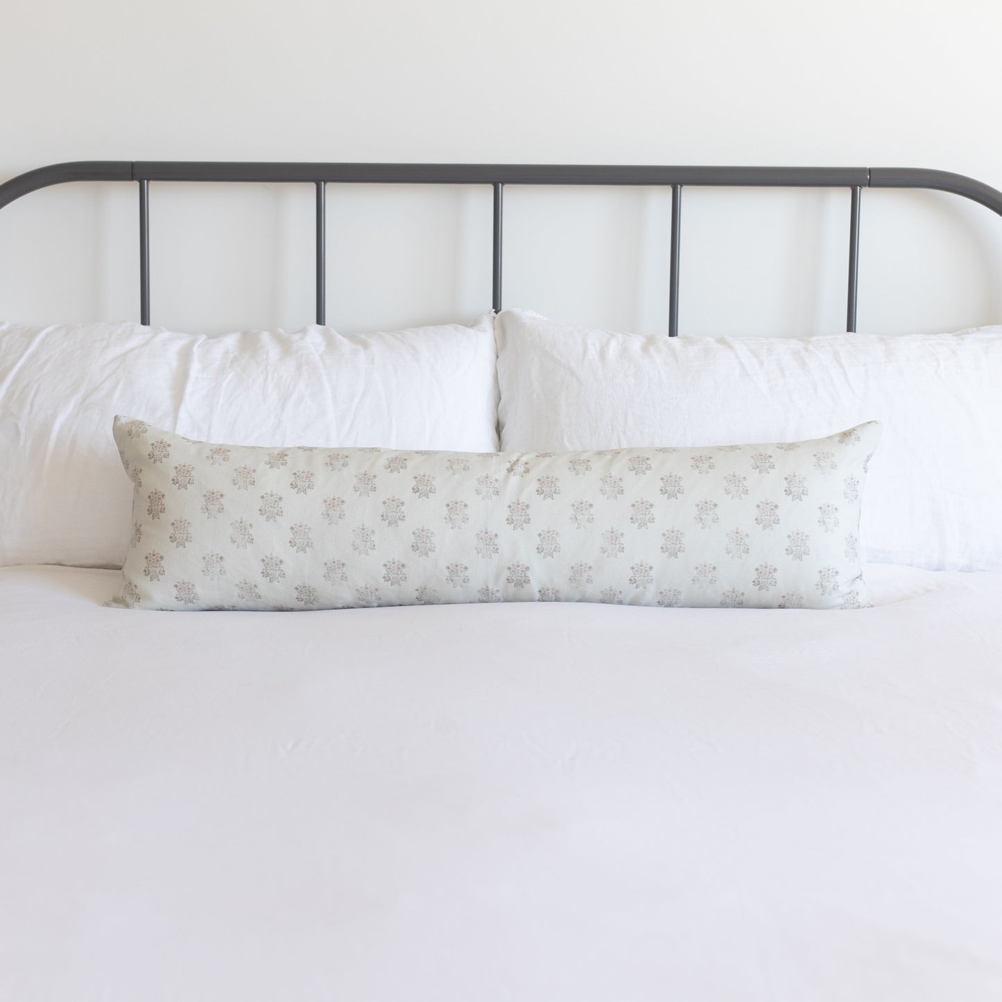 Long rectangular pillow with beige snowflake pattern displayed on bed with metal headboard and white bedding.
