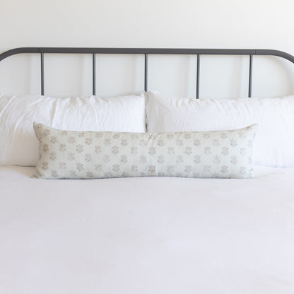 Long rectangular pillow with beige snowflake pattern displayed on bed with metal headboard and white bedding.
