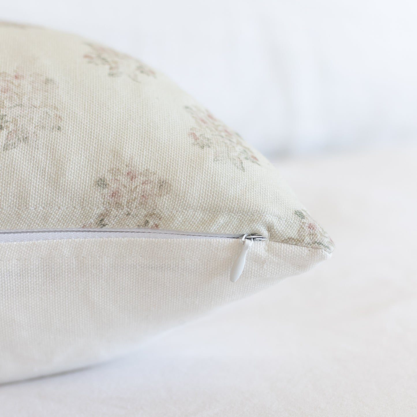 Cream lumbar pillow with faded botanical pattern and removable zipper cover.