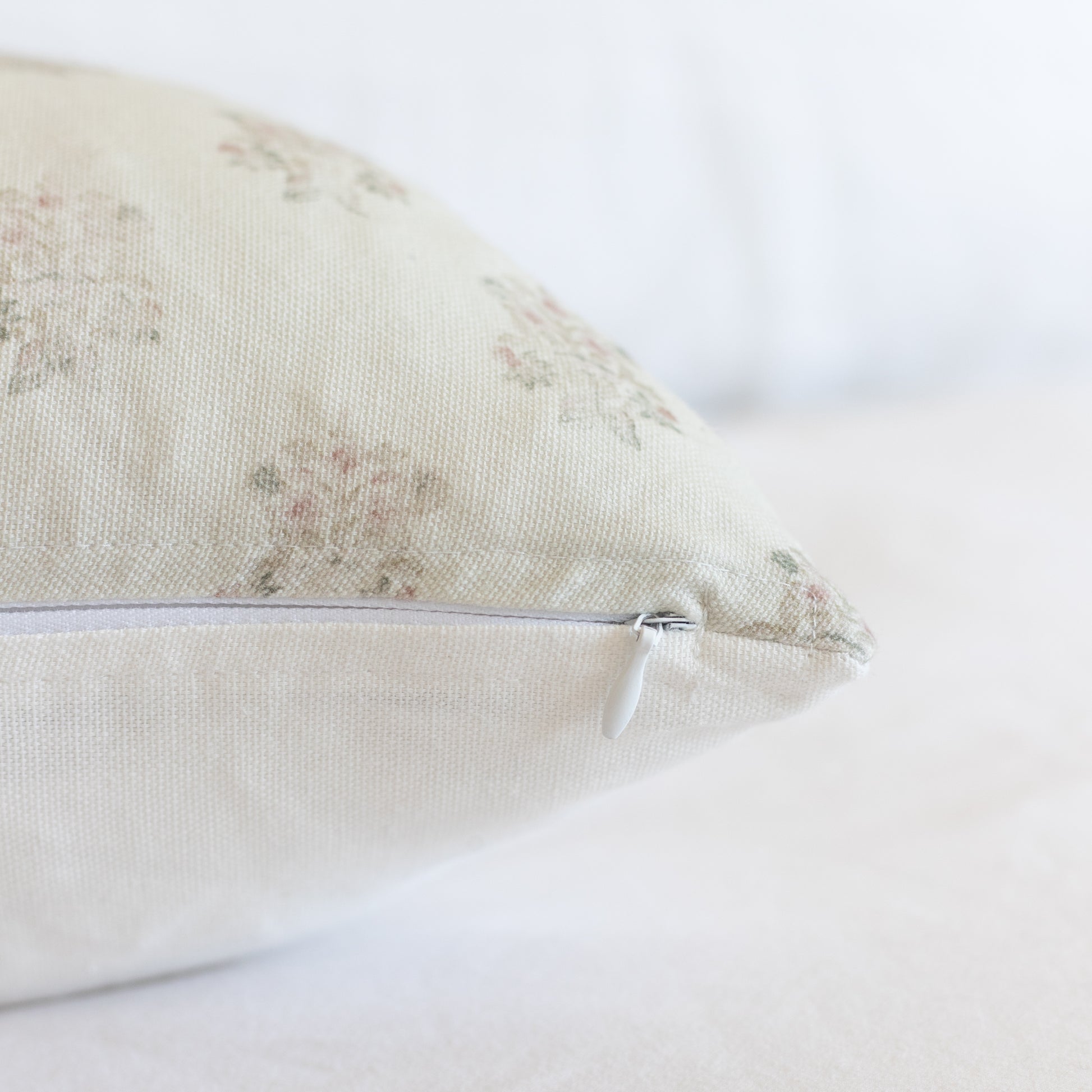 Cream lumbar pillow with faded botanical pattern and removable zipper cover.