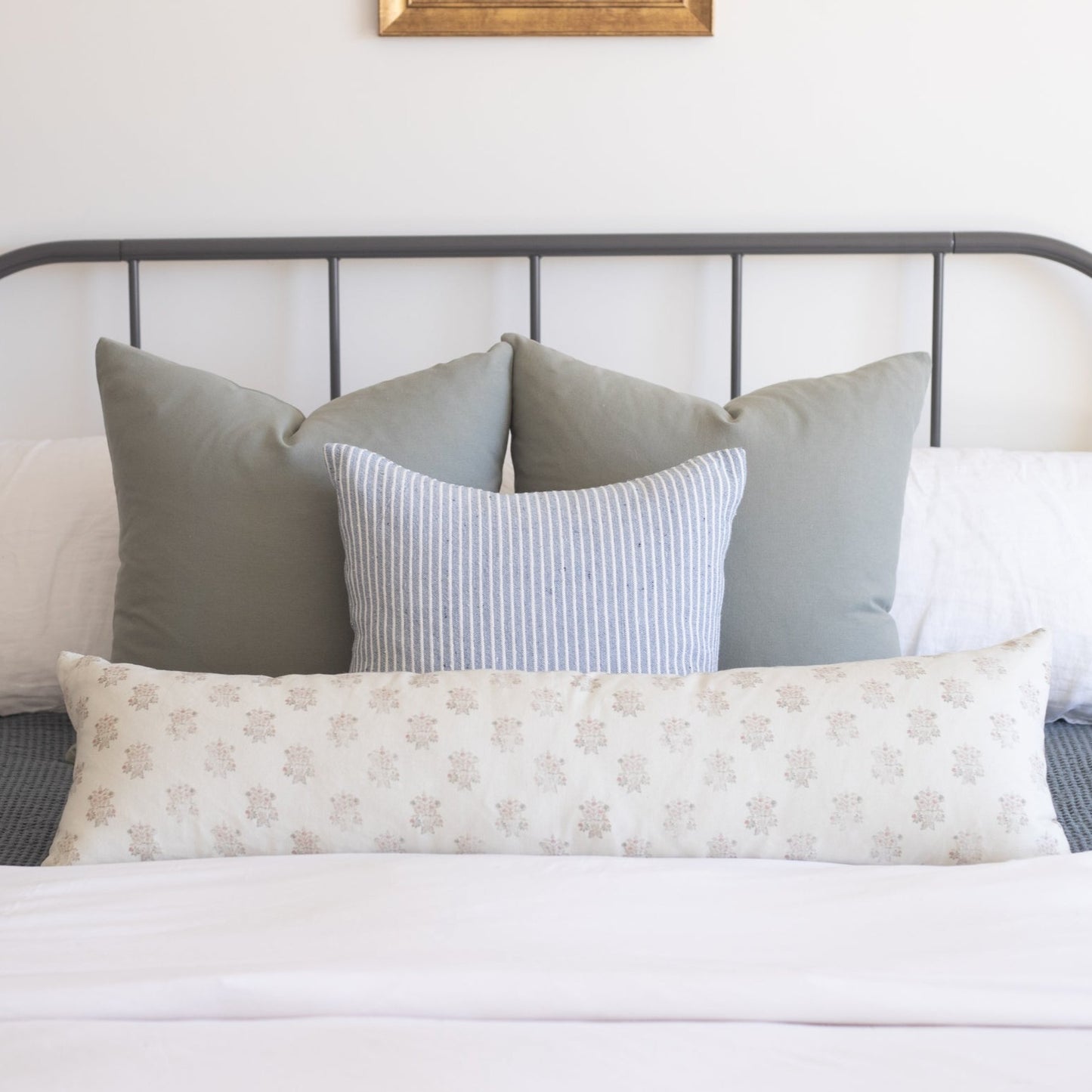 Rectangular lumbar pillow with cream background and small tan floral pattern displayed on a bed with gray and striped pillows