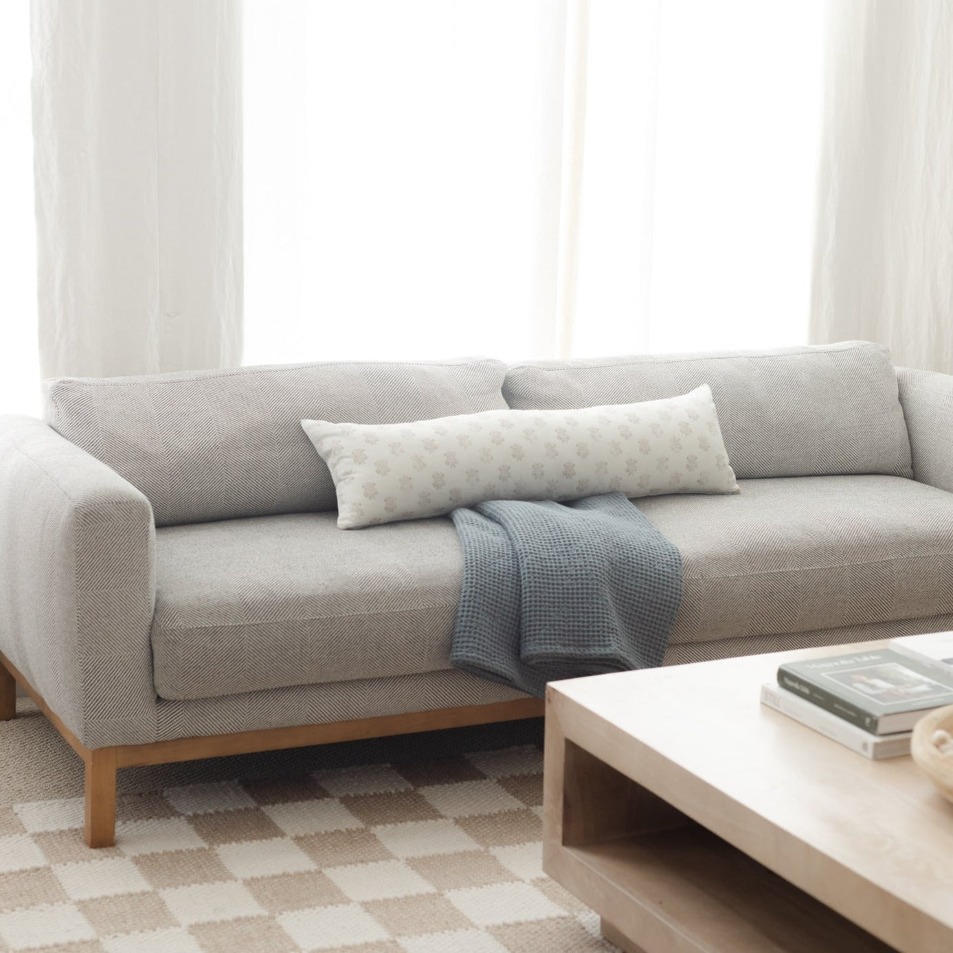 Light gray upholstered sofa with wooden legs, styled with white patterned and blue throw pillows and blanket.