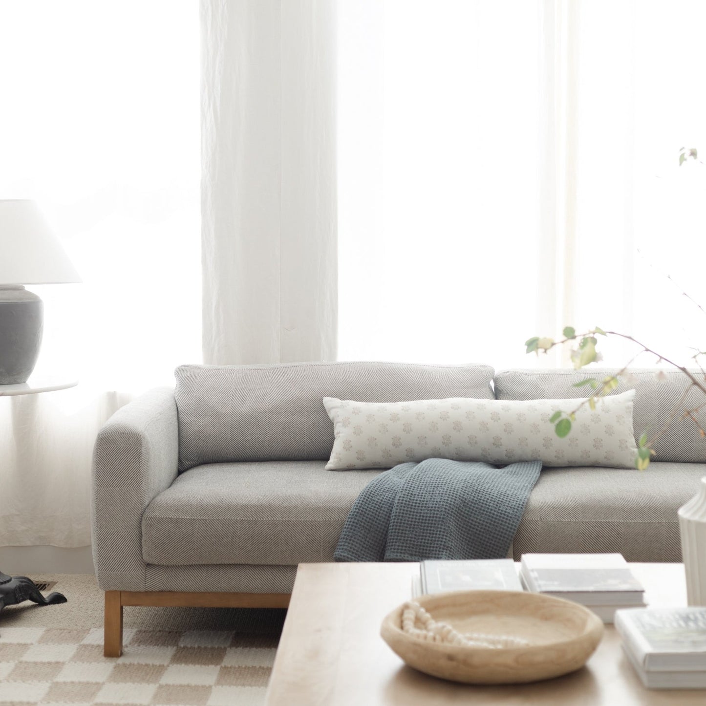 Cream and white patterned lumbar pillow on gray upholstered sofa with wooden legs.