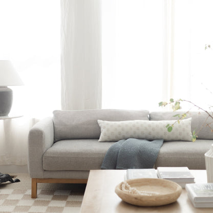 Cream and white patterned lumbar pillow on gray upholstered sofa with wooden legs.