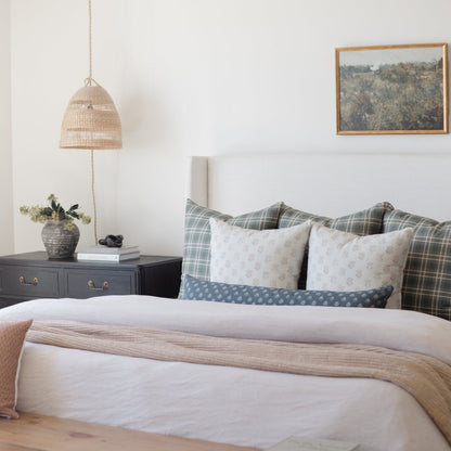 Woven pendant lamp with dome shape in natural rattan finish, suspended by cord over bedside table.