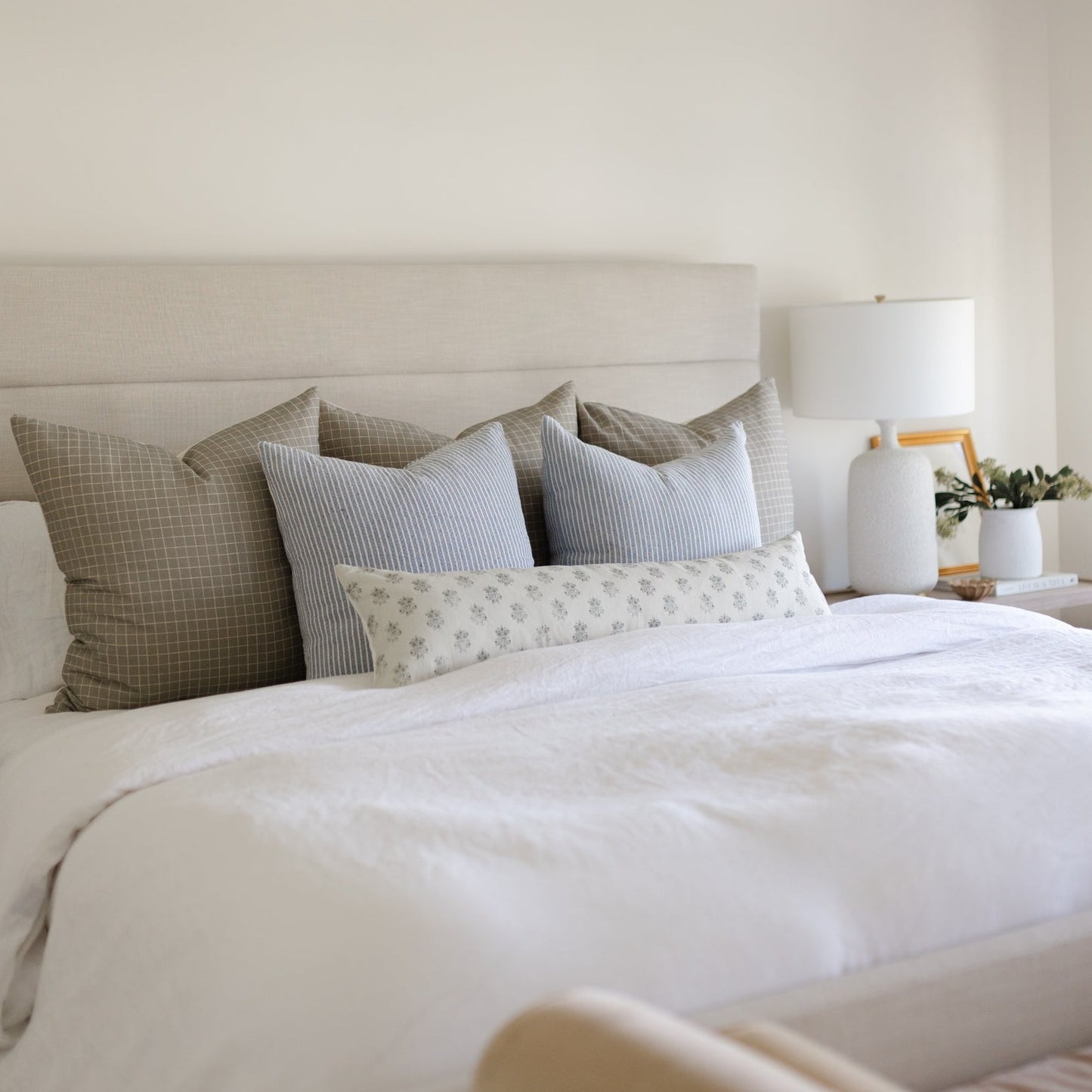 Blue ribbed decorative pillow displayed among neutral bedding and patterned throw pillows on a bed.