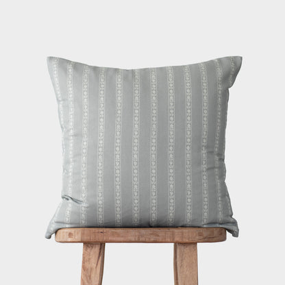 Gray and white striped throw pillow with geometric pattern displayed on wooden stool.