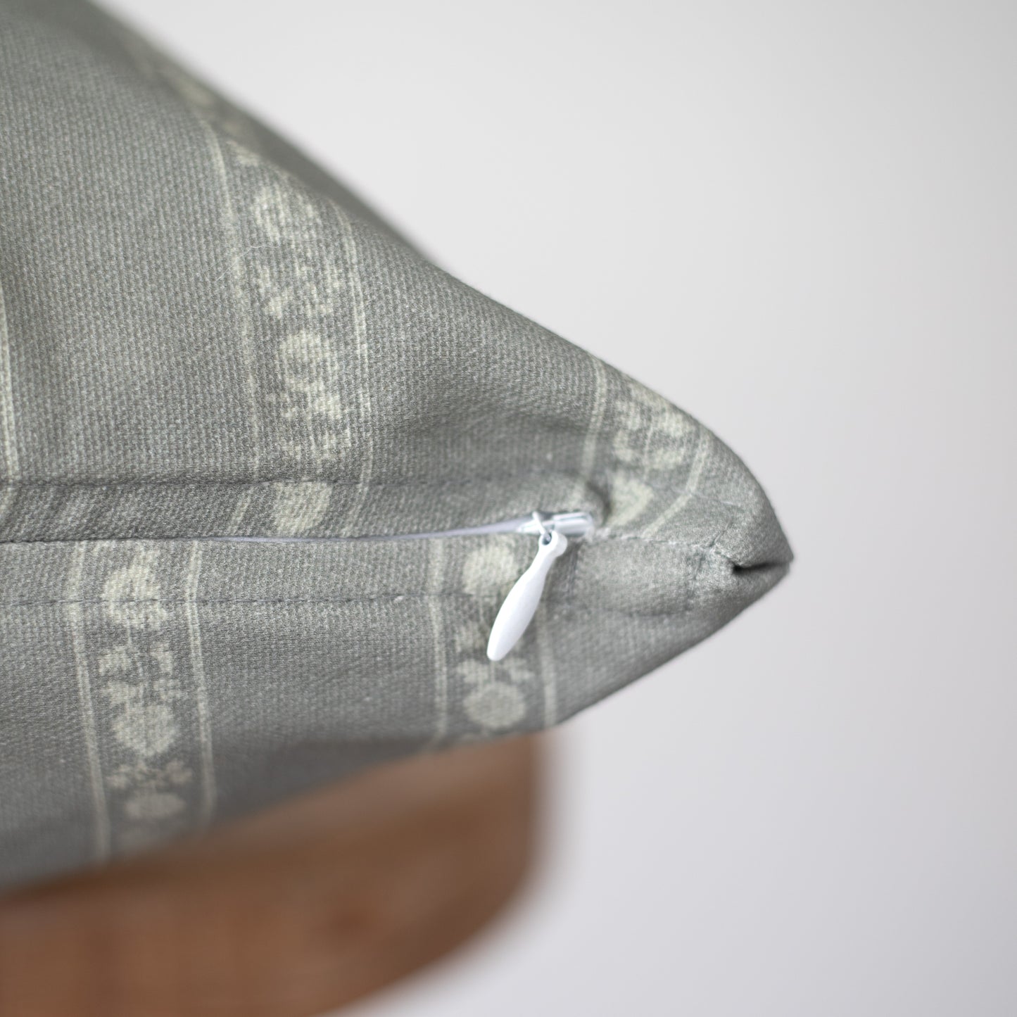 Gray woven pillow with geometric pattern and white zipper closure visible on seam.