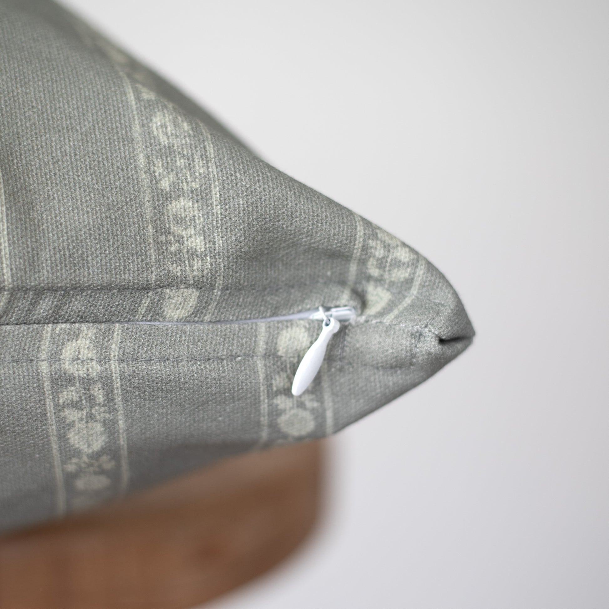 Gray woven pillow with geometric pattern and white zipper closure visible on seam.