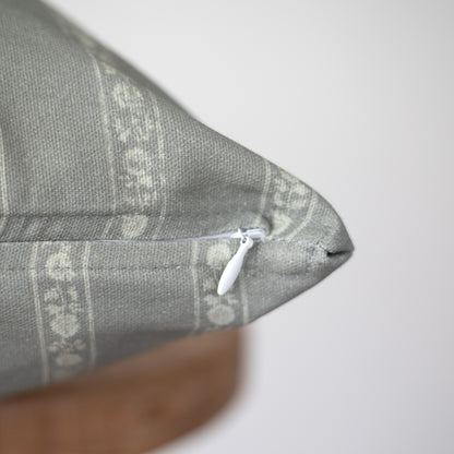 Gray woven pillow with geometric pattern and white zipper closure visible on seam.