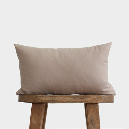 Tan rectangular lumbar pillow with solid color linen fabric displayed on wooden bench.