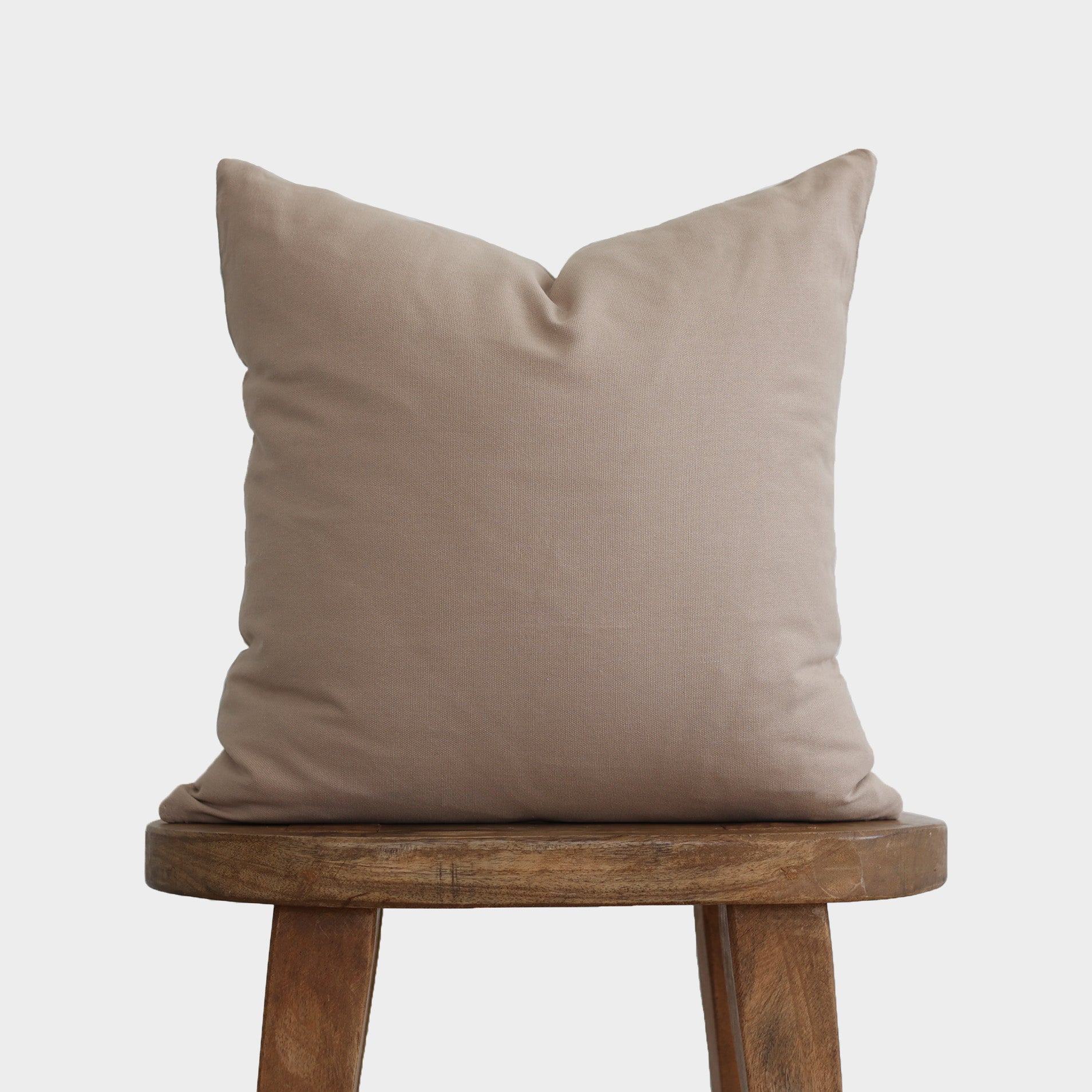 Tan linen pillow with envelope closure displayed on a wooden stool.