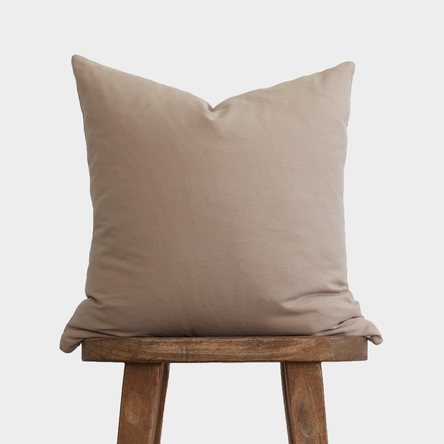 Tan linen pillow cover displayed on wooden stool, showing plain front with neutral solid color.
