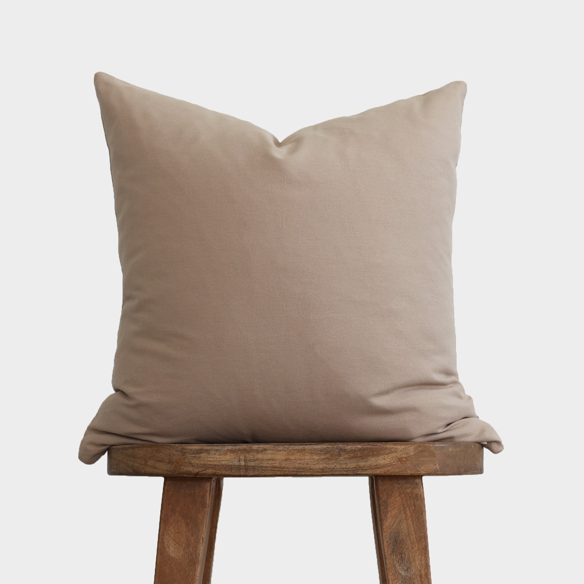 Tan linen pillow cover displayed on wooden stool, showing plain front with neutral solid color.