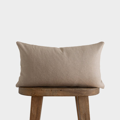 Beige boucle rectangular pillow with textured weave displayed on wooden chair.