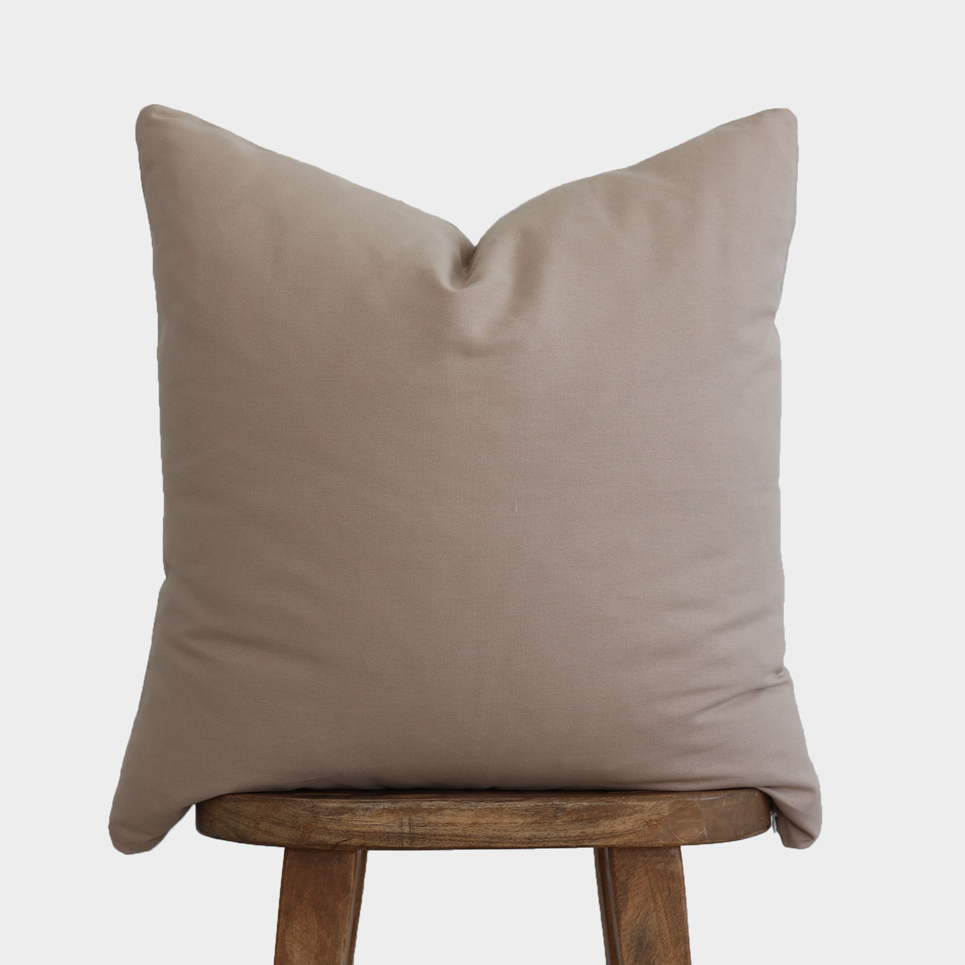 Tan solid pillow cover displayed on a wooden stool against a light background.