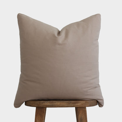 Tan solid pillow cover displayed on a wooden stool against a light background.