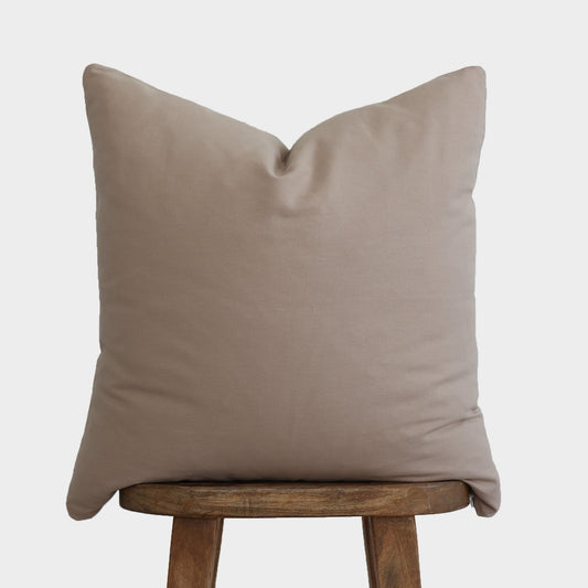 Tan solid pillow cover displayed on a wooden stool against a light background.