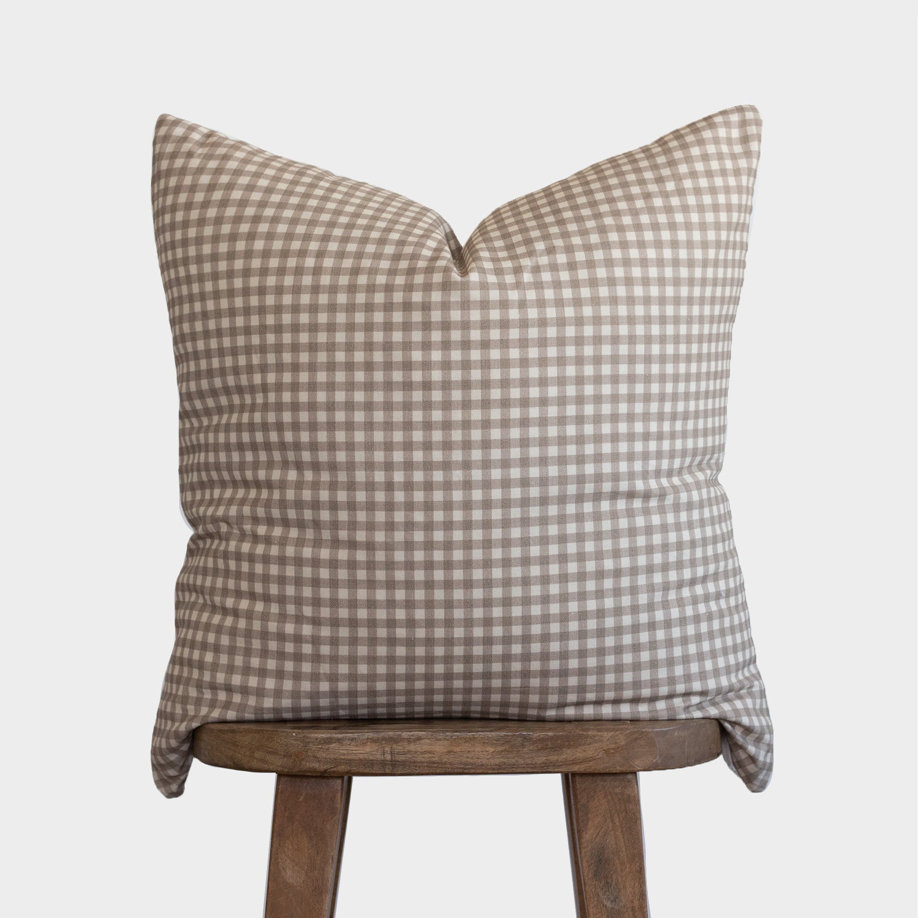 Tan and white gingham patterned pillow cover displayed on wooden stool.
