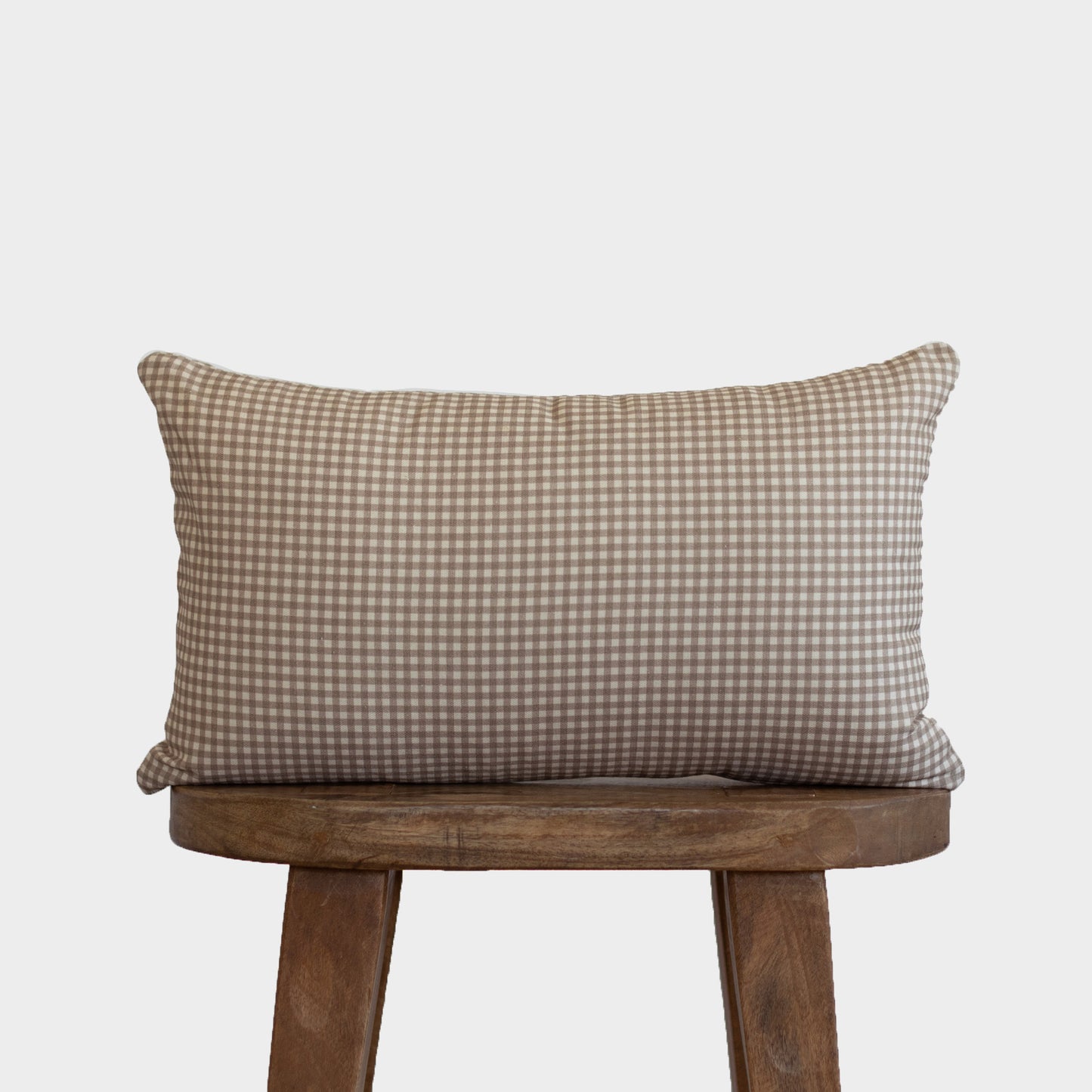 Tan and white mini gingham lumbar pillow displayed on a wooden chair.