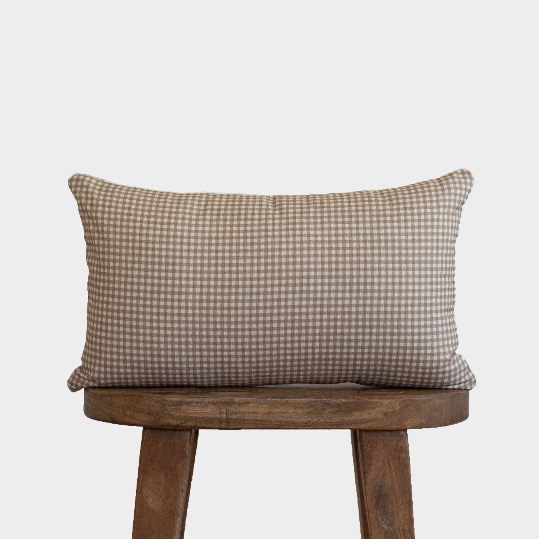 Tan and white mini gingham lumbar pillow displayed on a wooden chair.