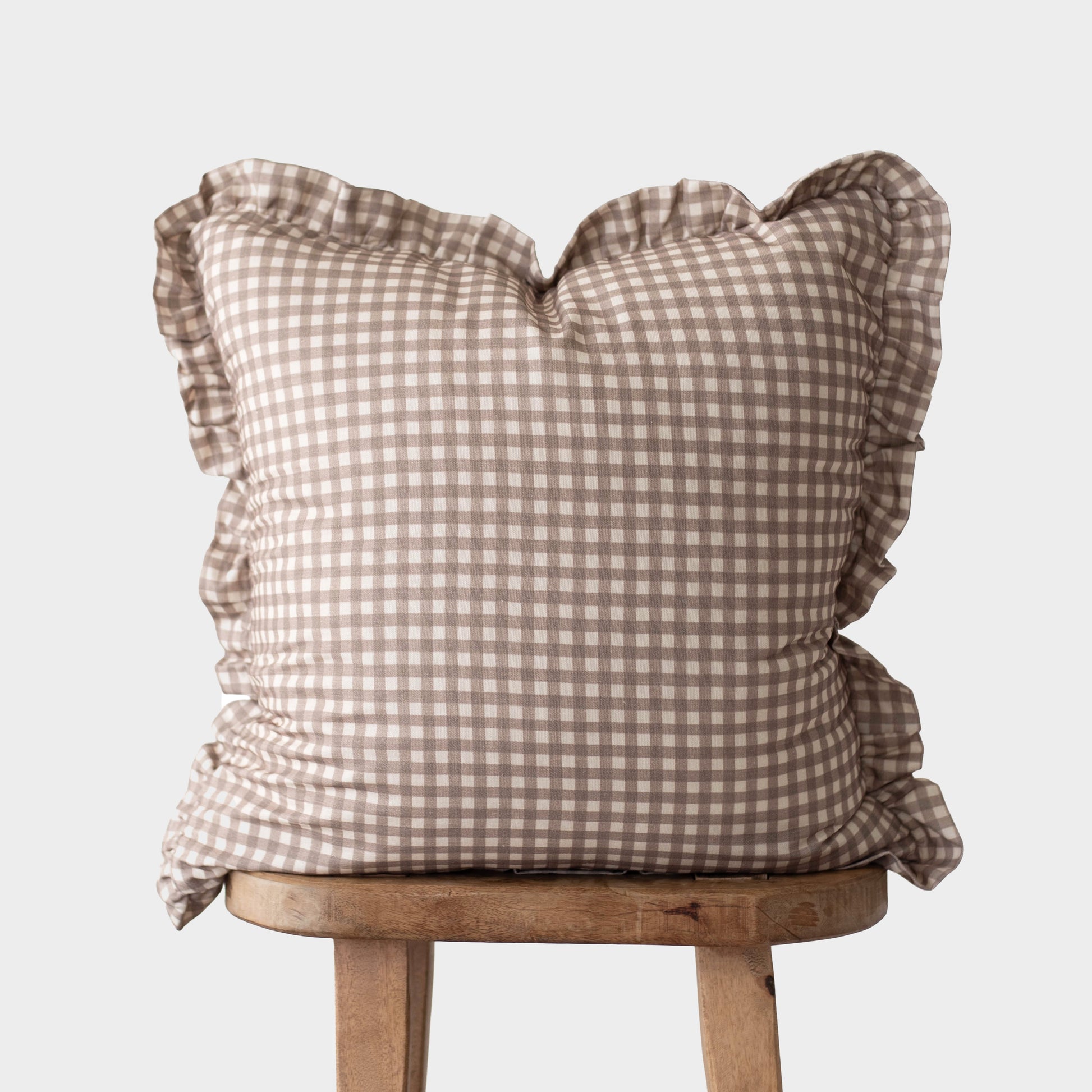 Tan and white gingham pillow with ruffled edges on all sides, displayed on a wooden stool.