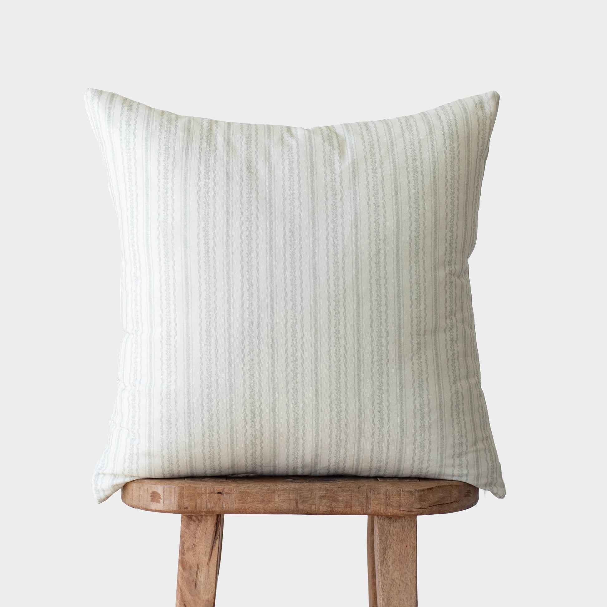 Cream and beige striped pillow cover displayed on wooden stool.