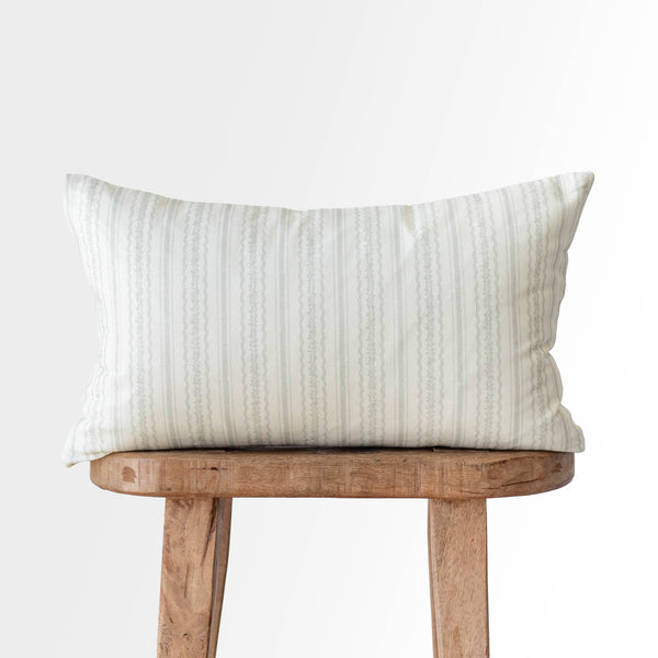 Cream and gray striped rectangular pillow with textured weave sitting on wooden stool.