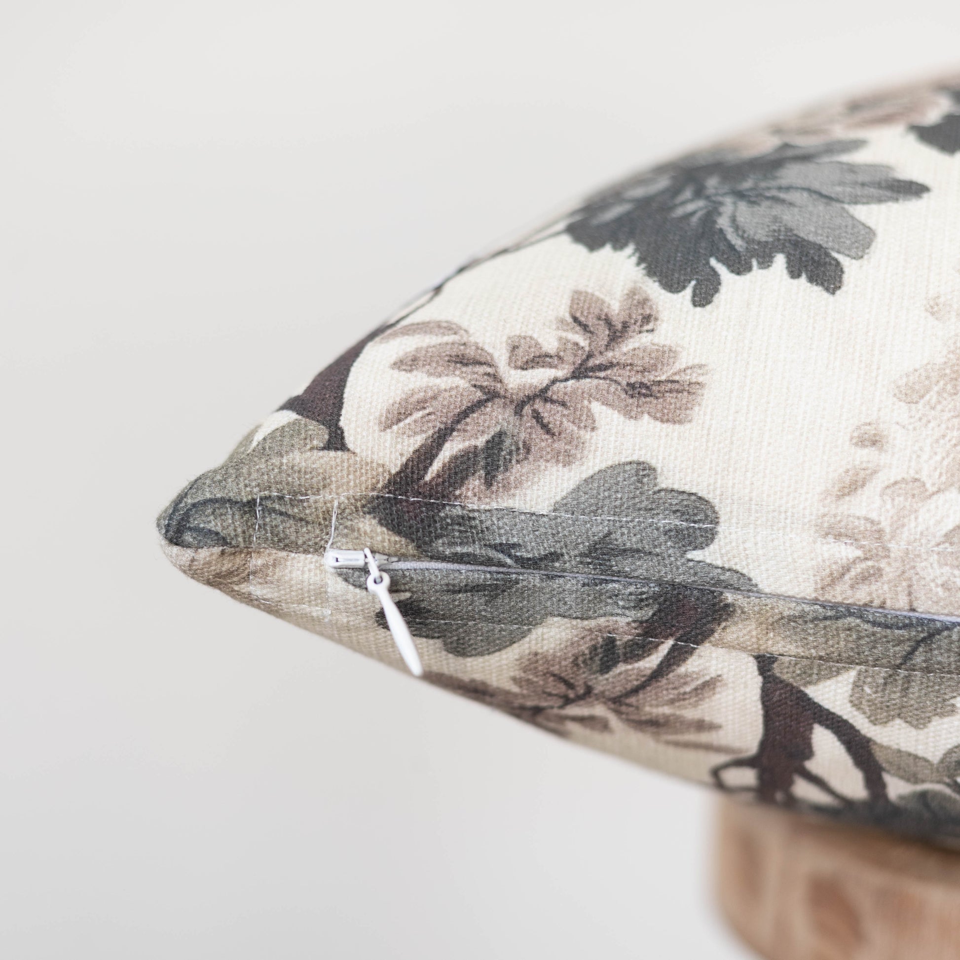 Fable pillow with floral botanical print in charcoal, taupe, and cream tones, featuring a white zipper closure.