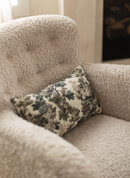 Cream textured throw pillow with green and black floral pattern resting on a beige upholstered chair.