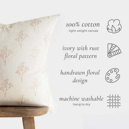 Rectangular lumbar pillow with rust-colored thistle pattern on ivory cotton canvas, displayed on wooden stool.