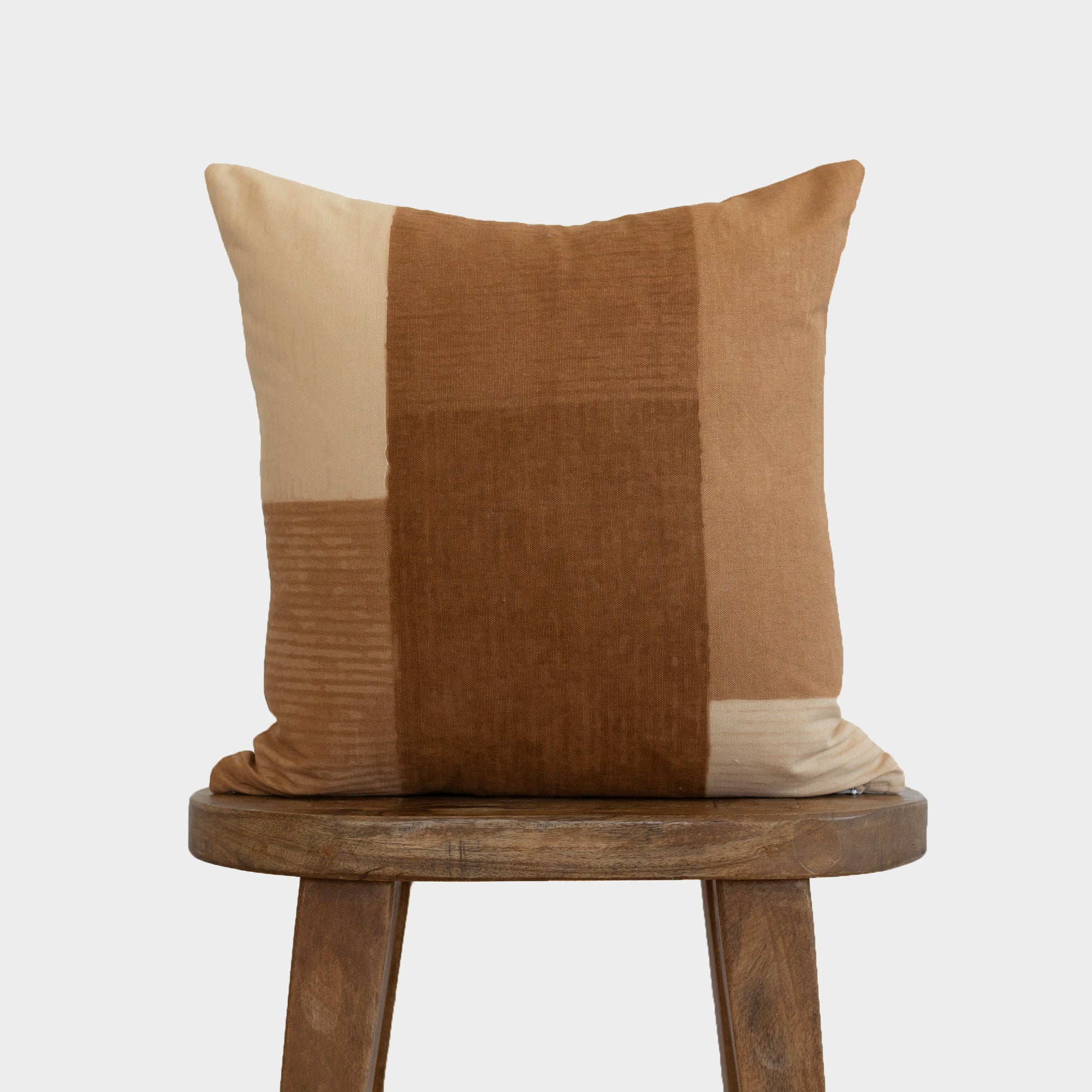 Tierra throw pillow with color-blocked design in cream, tan, and brown tones on wooden stool.