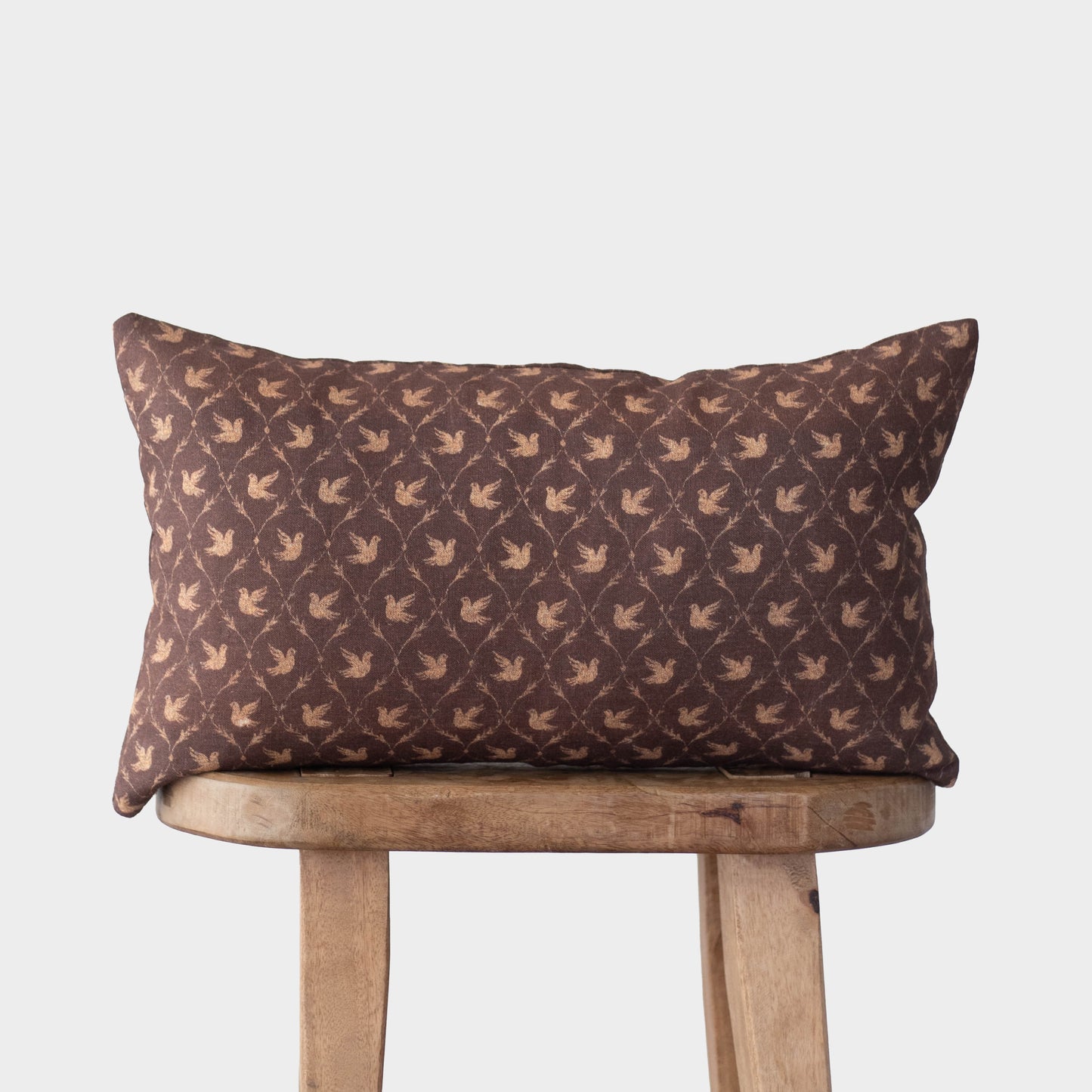 Brown rectangular pillow with repeating dove pattern in tan, displayed on wooden chair.