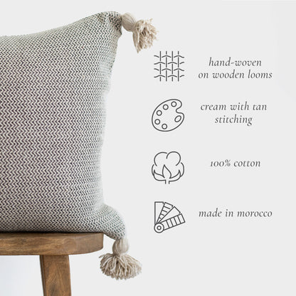 Cream and tan tweed pillow with chevron pattern and tassels on wooden stool.