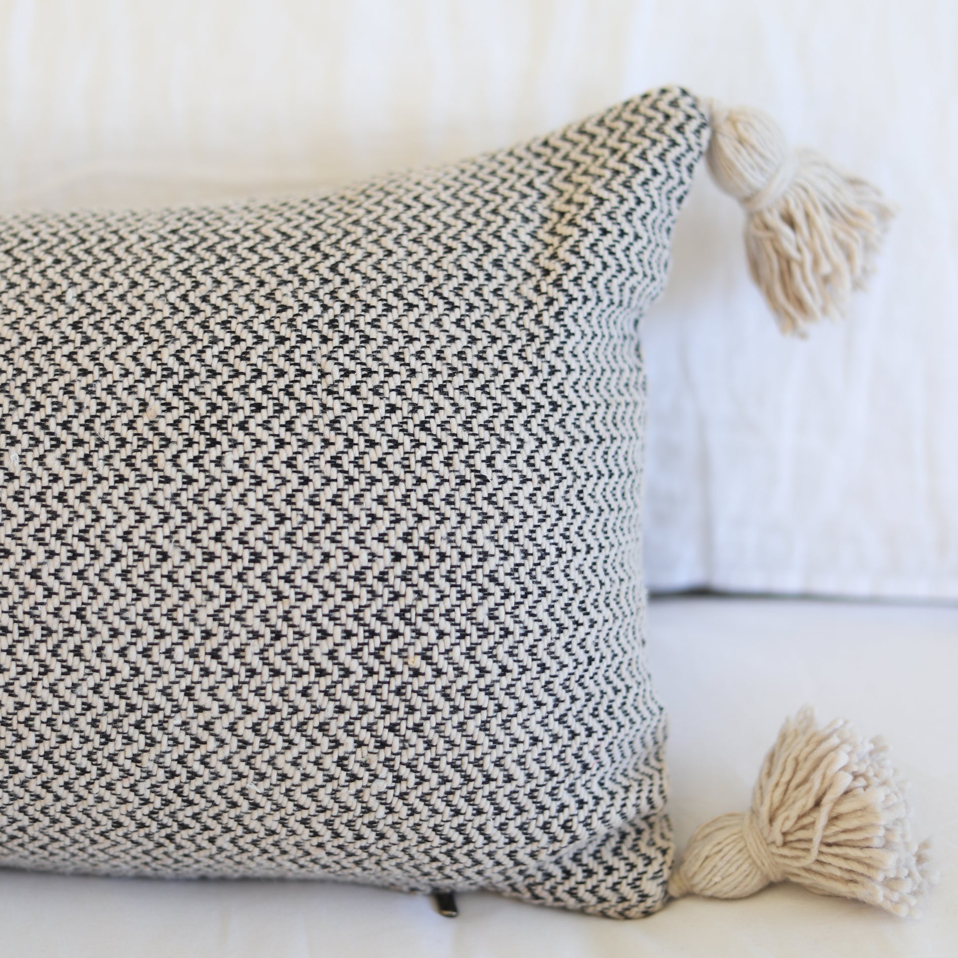Cream and charcoal tweed lumbar pillow with tassel corners and woven texture pattern.